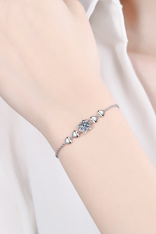 Model arm wearing rhodium plated sterling silver bracelet with two solid silver small hearts on either side of a round 1 carat Moissanite stone