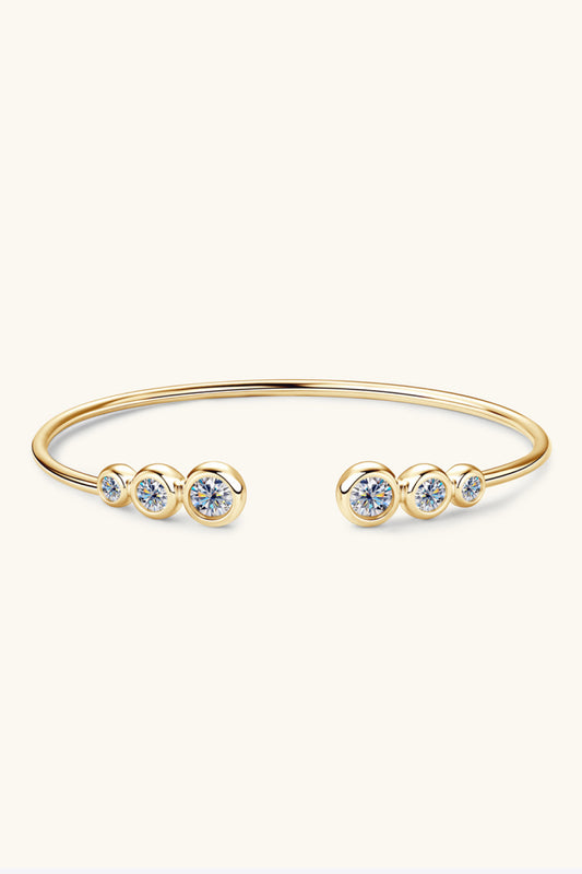 18k yellow gold plated sterling silver bracelet with cuff opening adorned by three round moissanite stones on the end of the opening on both sides on a white background. Also available in silver.
