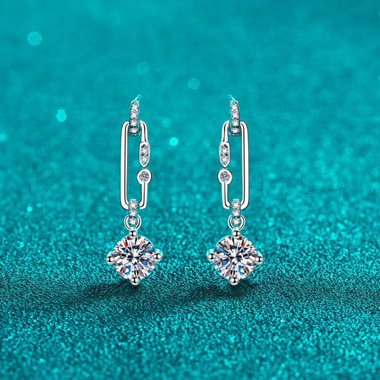 2 carat moissanite earrings in sterling silver with a pin dangle and 1 carat moissanite at the end of each earring against a teal backdrop.