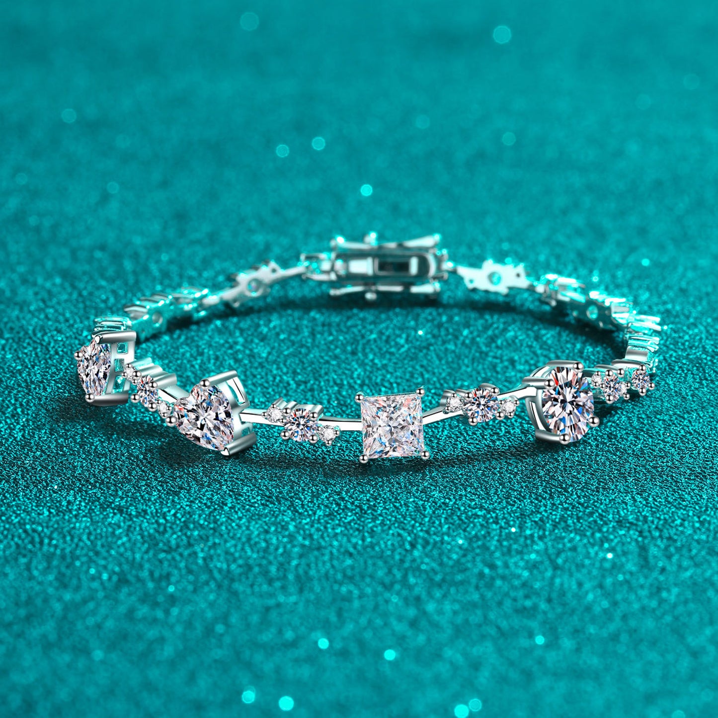 Sterling silver bracelet with 6.2 carats of moissanite in a variety of shapes on a teal background.