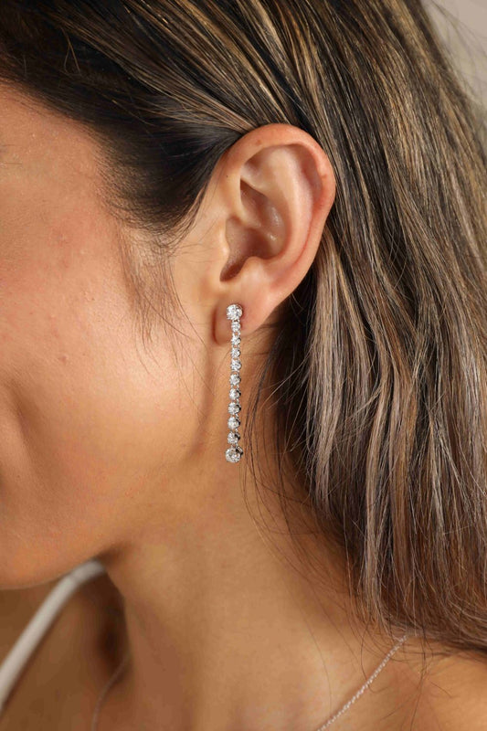 Woman with long brown hair wearing 1.18 carat long Moissanite earrings with a line of 11 small stones