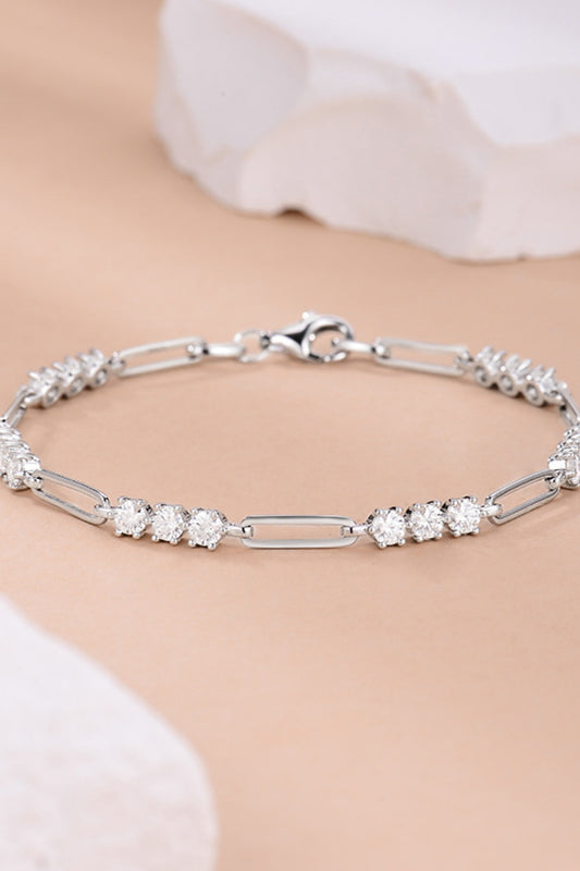 Platinum plated sterling silver moissanite bracelet with sets of three stones between long rectangular links on a peach background.