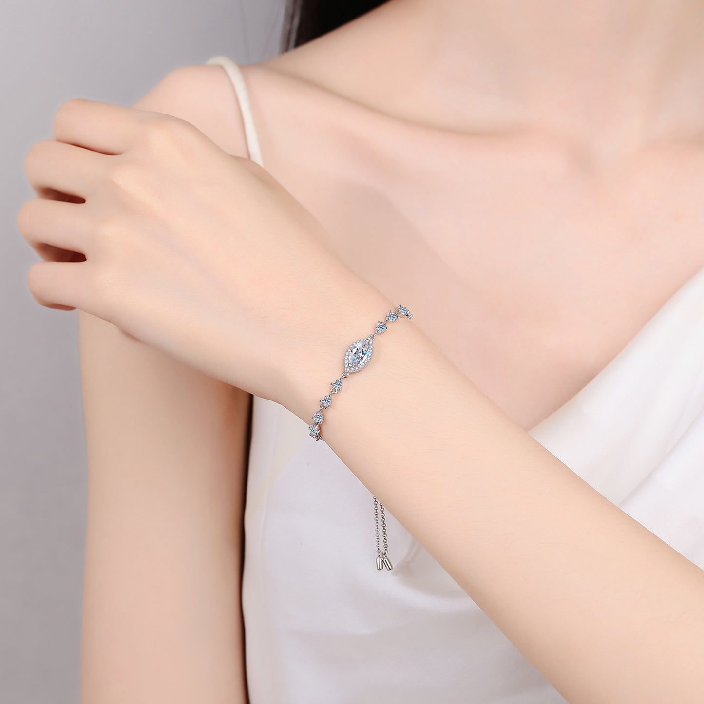 Woman wearing a beautiful moissanite bracelet with a marquis shaped center stone and smaller stones to both sides. 