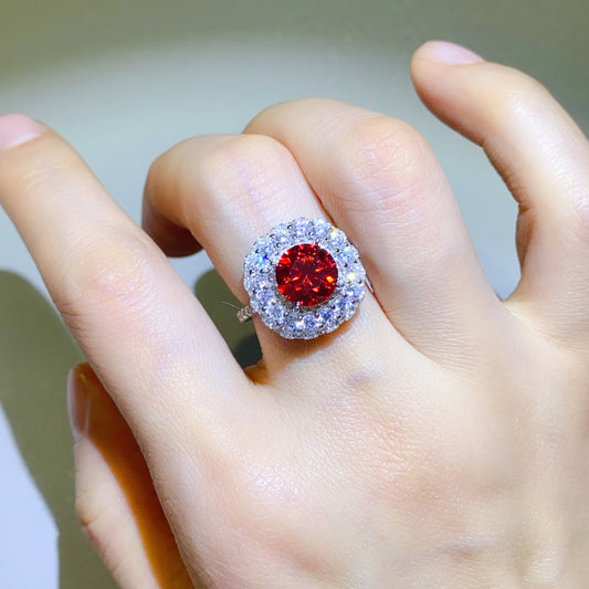 Model's hand wearing a sterling silver right with 2 carats of Moissanite. Large round red moissanite center stone surrounded by rows of white moissanite on a mint background.