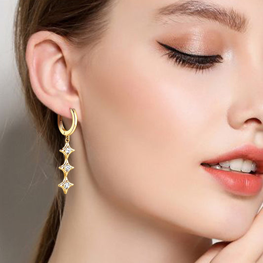 Model with light brown ponytail and coral lips wearing 18k yellow gold plated sterling silver earrings. Earrings have small hoops with three 4-pointed stars with a small moissanite in the center of each. 