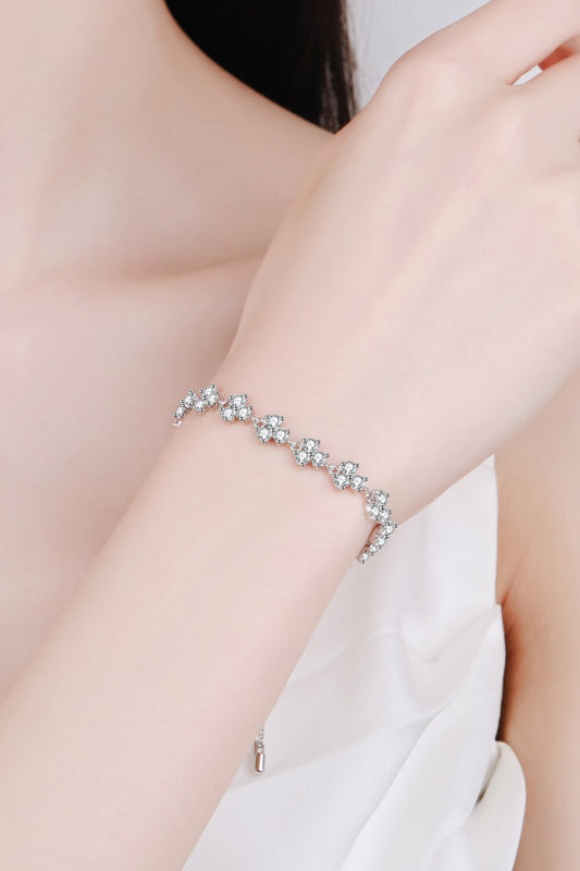 Adjustable rhodium plated sterling silver moissanite bracelet worn by a model with brown hair wearing a white top. Clusters of three small moissanite stones surround the bracelet.