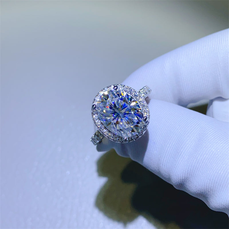 Hand wearing a white glove holding a 5 carat oval shaped moissanite ring on a white background.