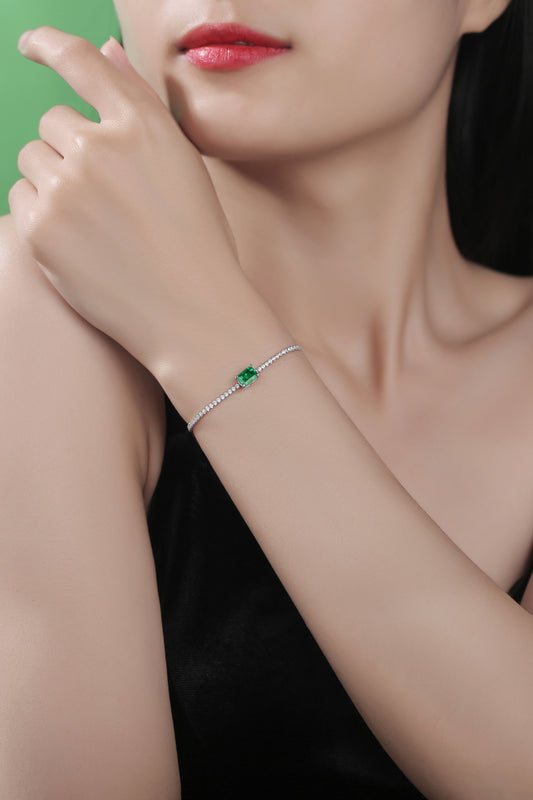 Woman with long dark hair and coral lipstick in a black dress wearing a zircon tennis bracelet with a rectangular lab created emerald in the center.  